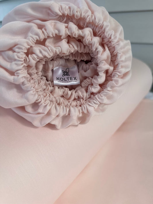 Pink satin headband with Koltex label on a light pink background