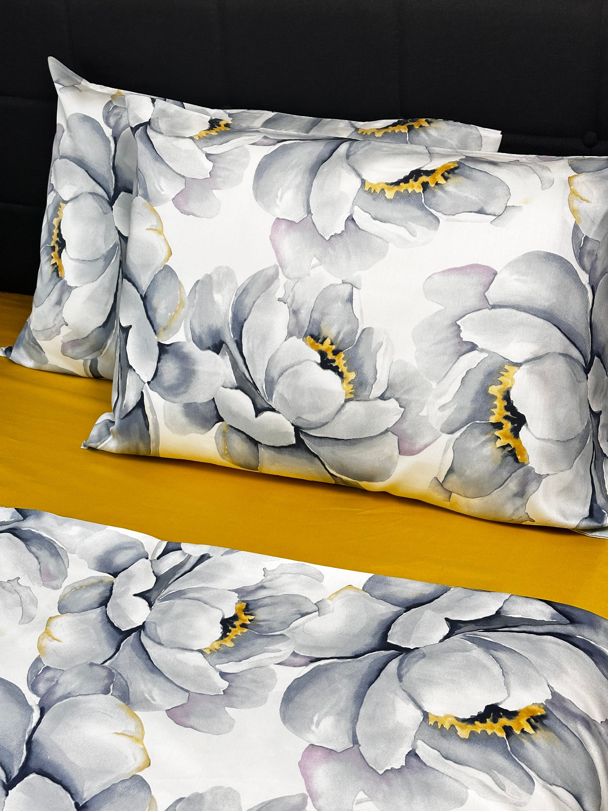 Chic bedroom decor with gray peony print pillowcases and duvet cover on a contrasting mustard sheet.