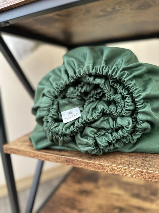 Rolled dark green organic cotton fitted sheet on wooden shelf