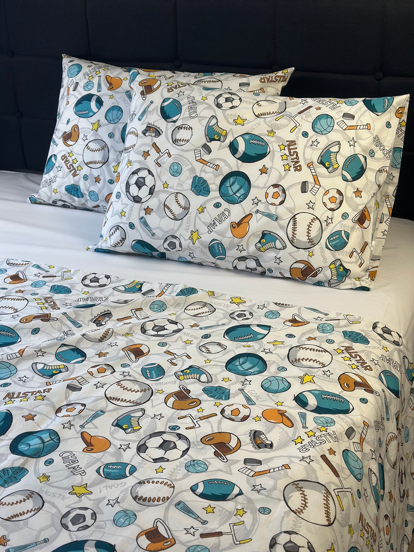 Children's sports-themed bedding set with pillows and sheet on a bed.