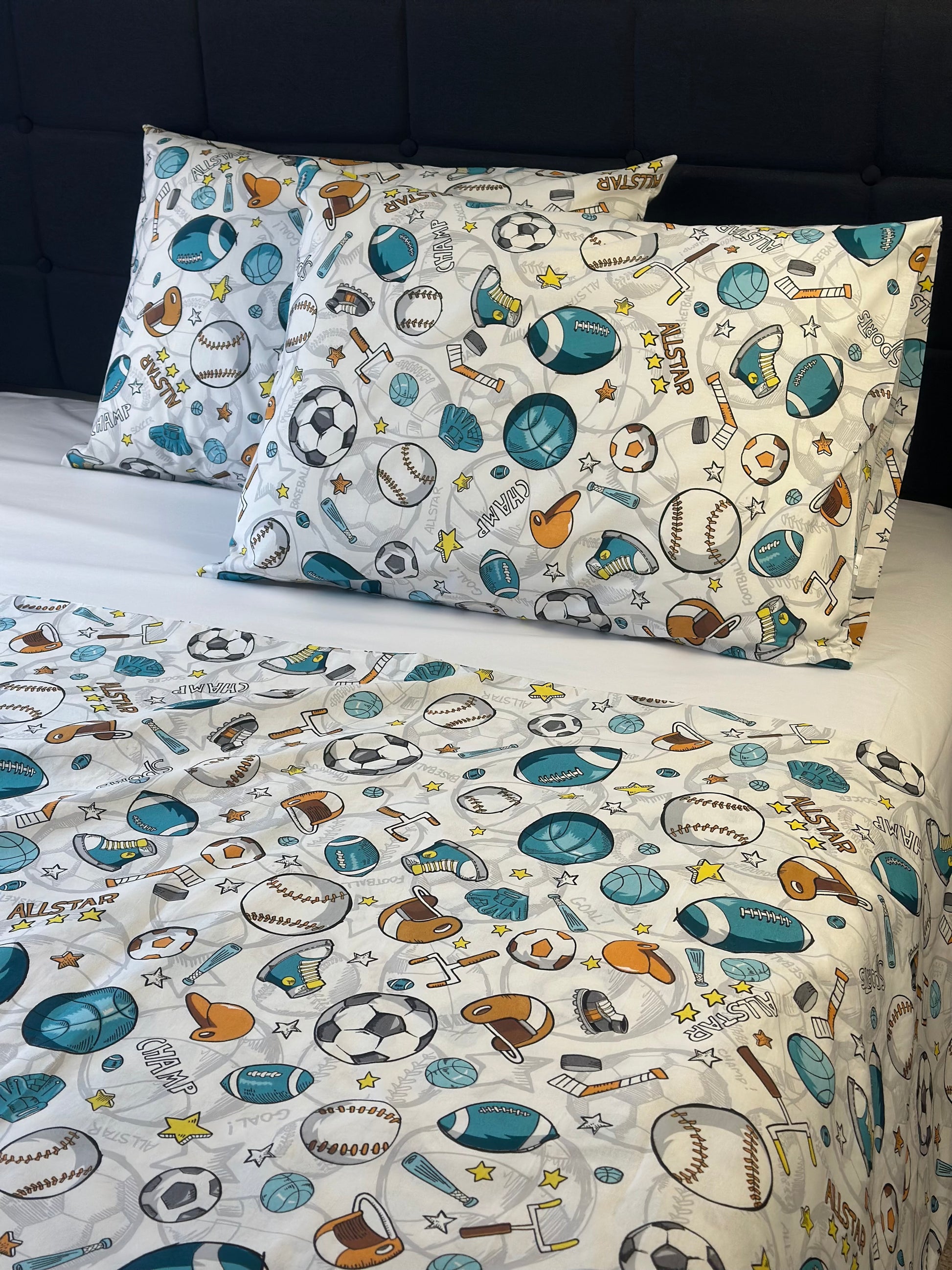 Children's sports-themed bedding set with pillows and sheet on a bed.